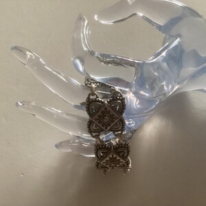 May include: Silver bracelet with a chain link design and decorative square charms. Each charm has a detailed floral pattern.