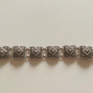 May include: A silver bracelet with a chain link design and square-shaped charms. Each charm has a detailed, intricate pattern.
