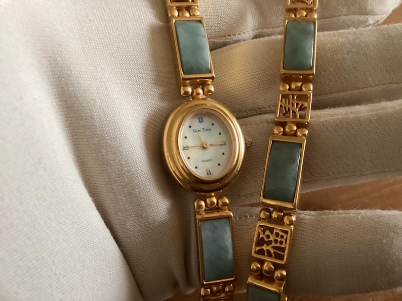 May include: Gold-toned quartz watch with a light blue jade-like stone and a white face. The watch has an oval face with Roman numerals and a matching bracelet. The watch is a quartz movement.