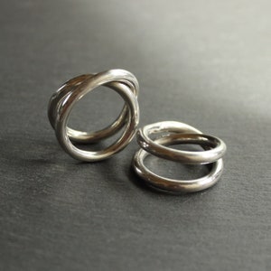 以下が含まれることがあります： 暗い灰色の表面に、3つのバンドが付いた銀のリングと、2つのバンドが付いた銀のリングが2つ置かれています。