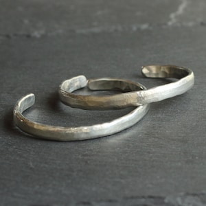 May include: Two silver bracelets with a hammered finish. The bracelets are stacked on top of each other.