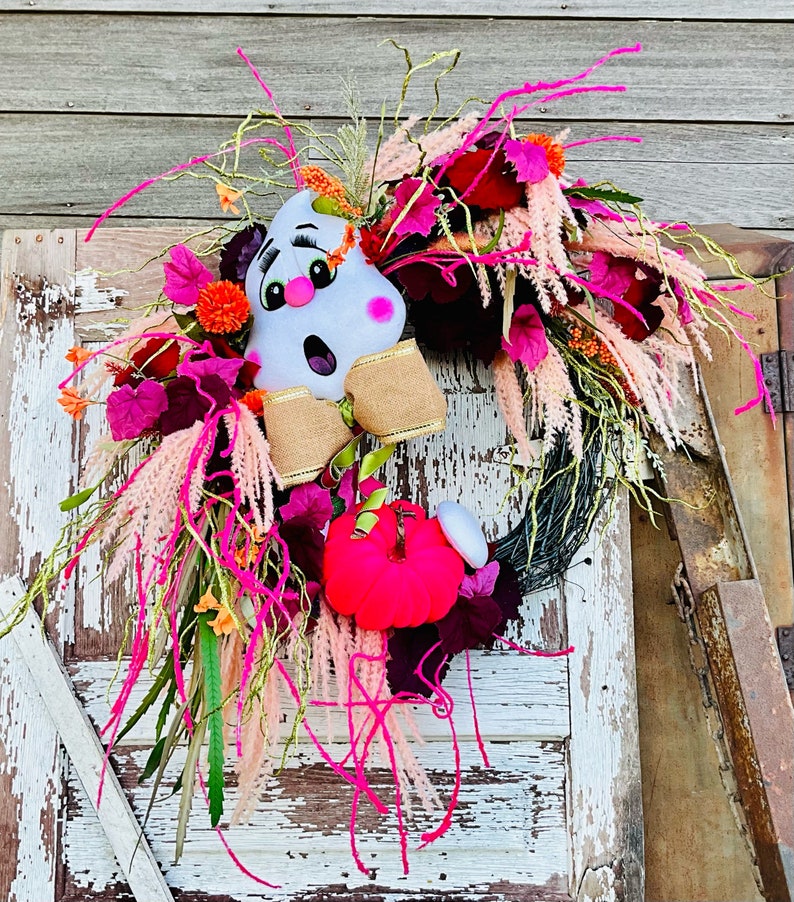 May include: A pink and white ghost with a pink pumpkin and pink and burgundy flowers on a wreath.
