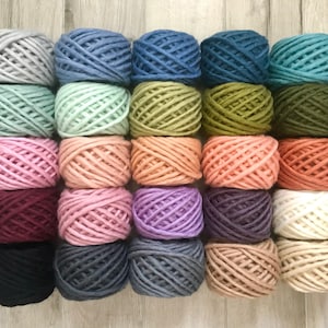 May include: A collection of twenty-five yarn balls arranged in a five-by-five grid. The yarn balls feature a diverse palette including shades of gray, blue, teal, green, pink, peach, orange, burgundy, purple, black, and cream colors.