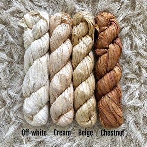 May include: Four twisted skeins of raffia ribbon arranged vertically. The colors from left to right are labeled as Off-white, Cream, Beige, and Chestnut. Each skein features a textured, fibrous appearance with a natural matte finish and consistent twist.