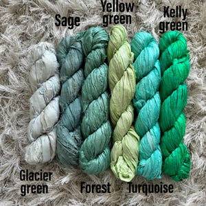 May include: Five skeins of textured ribbon yarn arranged side by side in a gradient of green shades. The colors are labeled as Glacier green, Sage, Forest, Yellow green, Turquoise, and Kelly green, showing a variety of light to dark tones.