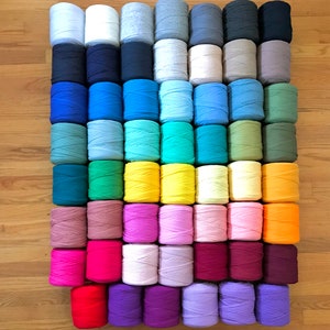 May include: A collection of colorful yarn spools arranged in a grid pattern. The spools display a variety of colors, including white, blue, green, yellow, pink, orange, and purple. The yarn is neatly wound, suggesting a craft or textile project.