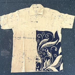 May include: A short-sleeved button-down shirt with a beige background and a navy blue and white floral design on the left side. The shirt has a classic collar and a relaxed fit, suitable for casual wear.