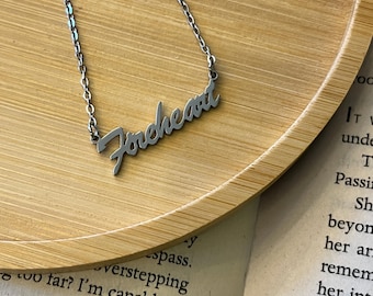 May include: A silver-toned metal necklace featuring a cursive script pendant that reads "Foreheart". The pendant is attached to a delicate link chain, showcasing a polished finish and a clean, legible font style for the lettering.