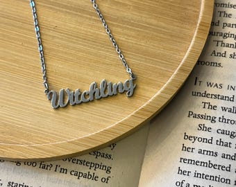 May include: A silver-toned metal necklace featuring a script-style nameplate pendant that reads Witchling. The pendant is attached to a delicate, thin link chain, creating a simple and clear piece of jewelry for the neck.