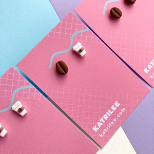 Pode incluir: Três cartões cor-de-rosa com um padrão de grade. Cada cartão tem um pequeno charme de xícara de café e grão de café. Os cartões têm o texto "Katrilee" e "katrilee.com" impresso neles.