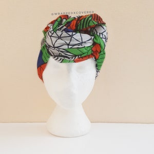 Op de afbeelding: Een groene, oranje, blauwe en witte geprinte hoofdband geknoopt op een wit mannequin hoofd. De tekst "FULLSIZE: NEVER ENDING" is afgedrukt onder het mannequin.