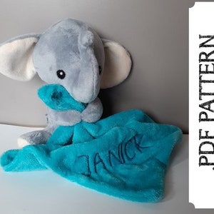 Könnte beinhalten: Ein graues Plüsch-Elefantenspielzeug hält eine türkisblaue Decke mit dem Namen "Janick" bestickt.