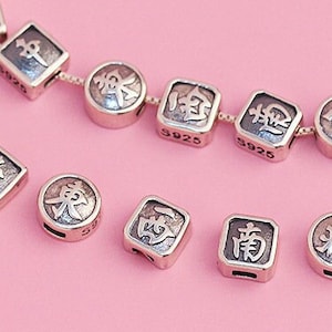 May include: Silver charm beads with Chinese characters on a pink background. The beads are square and round in shape. The beads are for jewelry making.
