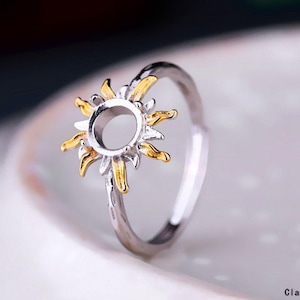 May include: A silver ring featuring a gold sun design. The centre of the sun is a round, open space for a stone or other embellishment.