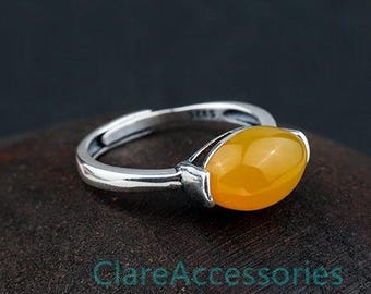 May include: A silver ring featuring a smooth, oval-shaped yellow gemstone set in a polished metal band. The band has an open, adjustable design at the back and is stamped with the text S925. The text ClareAccessories is visible below the ring.