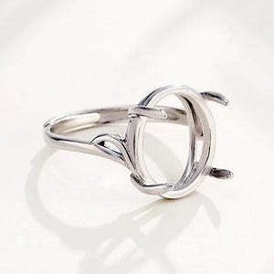 May include: A silver-toned metal ring setting featuring an oval-shaped prong mount designed to hold a gemstone. The band displays a delicate, openwork leaf-like detail on the sides, leading up to the four prongs that extend upwards from the centre.