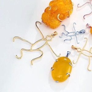May include: A collection of jewelry components including yellow amber-colored stone pendants and metal spider-shaped settings. The metal frames are gold and silver-toned, featuring long curved legs. The text ClareAccessories is visible at the top.