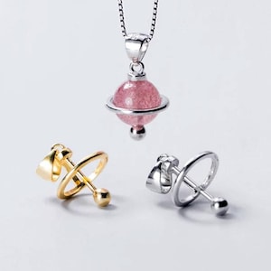 May include: A silver necklace featuring a round pink strawberry quartz pendant with a surrounding ring and a small sphere at the base. Below are two additional pendant settings, one in gold tone and one in silver tone, each with a ring and sphere.