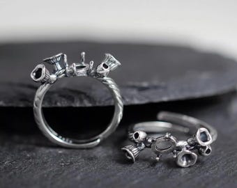 May include: Two silver rings with a floral design. The rings have a twisted band and are adorned with small, bell-shaped flowers and a central setting for a gemstone. The rings are displayed on a dark, textured surface.