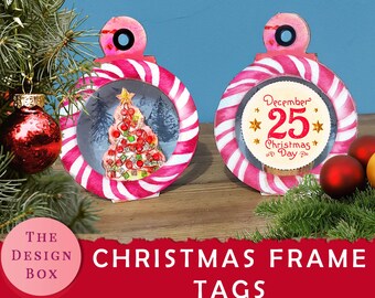 Puede incluir: Dos etiquetas de adorno de Navidad a rayas rosa y blancas. Una etiqueta tiene una escena de invierno con un árbol de Navidad en su interior. La otra etiqueta tiene un círculo con el texto "Diciembre 25 Navidad" en su interior.
