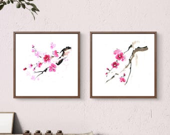 May include: Two framed watercolor paintings of pink cherry blossoms on a white background. The paintings are in brown frames and are hanging on a white wall.