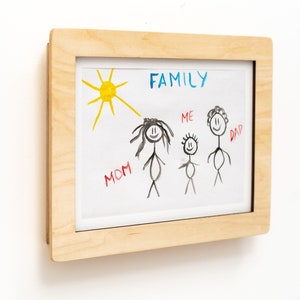 May include: A framed drawing of a family with the word "FAMILY" written in blue at the top. The drawing includes a sun, a mom, a dad, and a child labeled "ME".