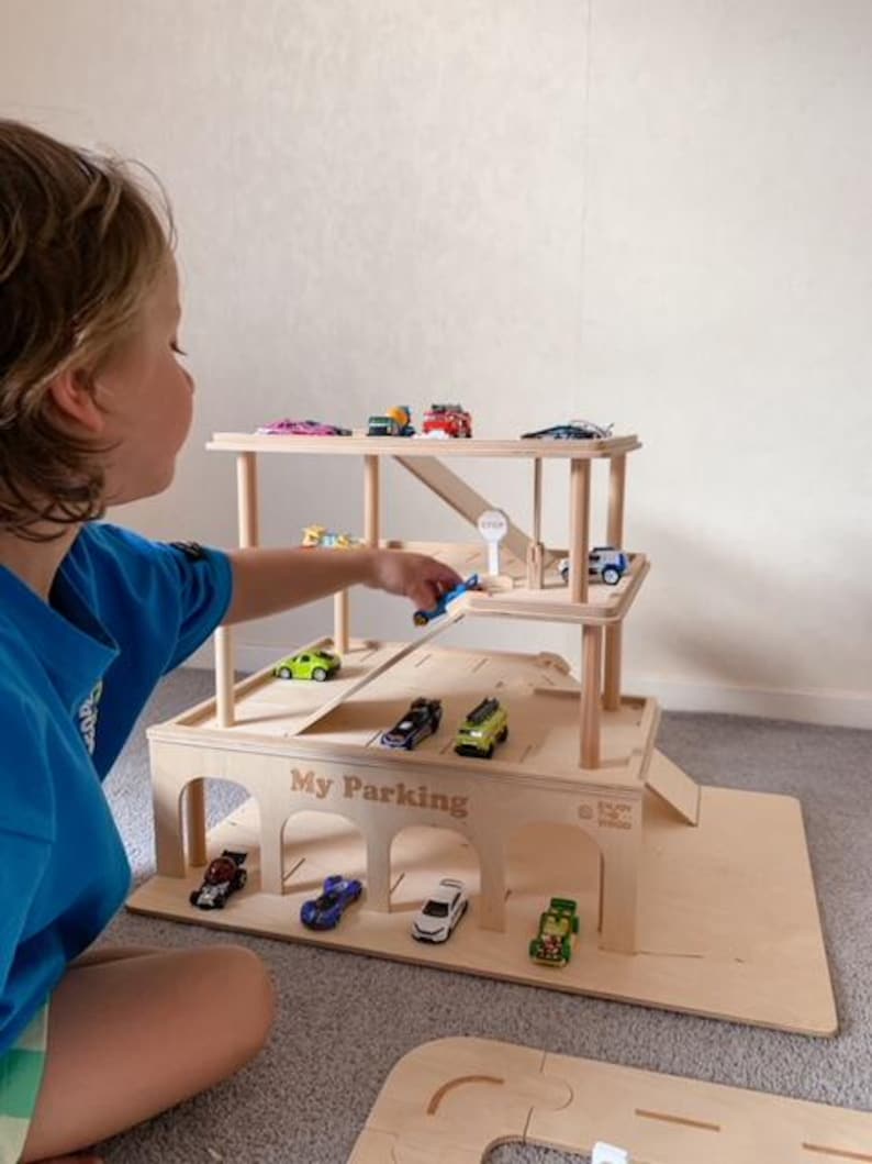 K&ouml;nnte beinhalten: Ein h&ouml;lzernes Spielzeug-Parkhaus mit mehreren Ebenen und Rampen. Das Parkhaus ist mit bunten Spielzeugautos gef&uuml;llt. Der Text "My Parking" ist auf der Vorderseite zu sehen. Das Spielzeug ist aus hellem Holz gefertigt.
