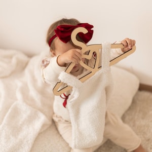 Puede incluir: Un ni&ntilde;o sostiene una percha de madera con un recorte en forma de coraz&oacute;n. La percha est&aacute; decorada con un lazo de terciopelo rojo. El ni&ntilde;o lleva un su&eacute;ter blanco peludo y una diadema de terciopelo rojo.