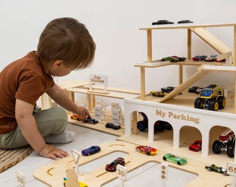 Könnte beinhalten: Ein mehrstöckiges Parkhaus aus Holz mit weißen Bögen und der Aufschrift My Parking, inklusive einer angeschlossenen Tankstelle, Rampen und verschiedenen kleinen Spielzeugautos, die auf der Struktur und den hölzernen Straßenteilen stehen.