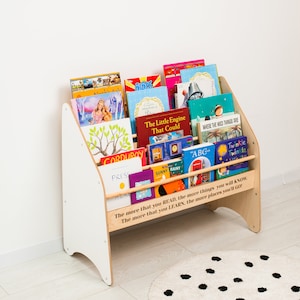 May include: A wooden children's bookshelf with white side panels and natural wood shelves. The front features the quote: The more that you READ, the more things you will KNOW. The more that you LEARN, the more places you'll GO! It is filled with various colorful books.