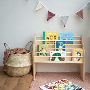 May include: A light-colored wooden bookshelf holding children's books with colorful covers, a woven seagrass basket with a brown cloth, and a wooden alphabet puzzle board with individual letter pieces scattered nearby.
