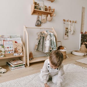 May include: A child plays with a red toy car on a white fluffy rug in a room with a wooden coat rack and shelves. The shelves are decorated with wooden toys and a sign that says "Leo".