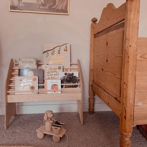 May include: A light-colored wooden bookshelf holding several children's books with titles including Slow Down, The Very Cranky Bear, and Treasured Tales from Beatrix Potter. A wooden pull-toy dog with a xylophone sits on the floor in front of the shelf.