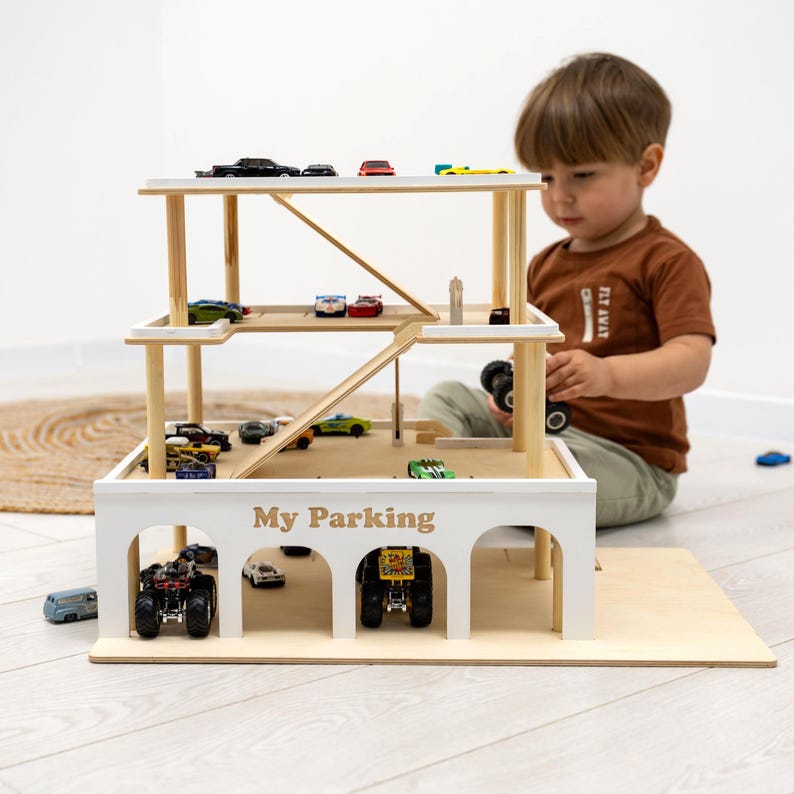 K&ouml;nnte beinhalten: Ein mehrst&ouml;ckiges Parkhaus aus Holz mit wei&szlig;em &Auml;u&szlig;eren und Akzenten aus Naturholz. Das Parkhaus hat mehrere Ebenen mit Rampen und Parkpl&auml;tzen, die mit Spielzeugautos gef&uuml;llt sind. Der Text "My Parking" ist auf der Vorderseite aufgedruckt.