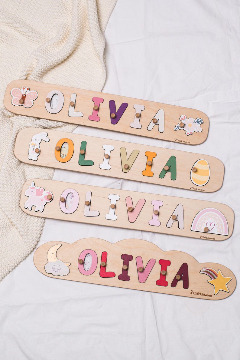 May include: Wooden name puzzles spelling "Olivia" in various pastel colors. Each puzzle features a different decorative element, including a butterfly, bunny, unicorn, and cloud. The puzzles are designed for children.