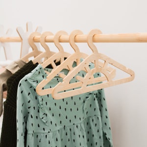 May include: Wooden hangers with a sun design, hanging on a wooden rod. A green dress with black polka dots is hanging on the hangers.