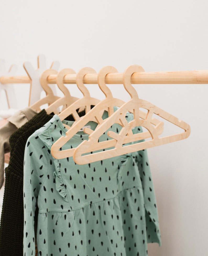 May include: Wooden hangers with a sun design, hanging on a wooden rod. A green dress with black polka dots is hanging on the hangers.