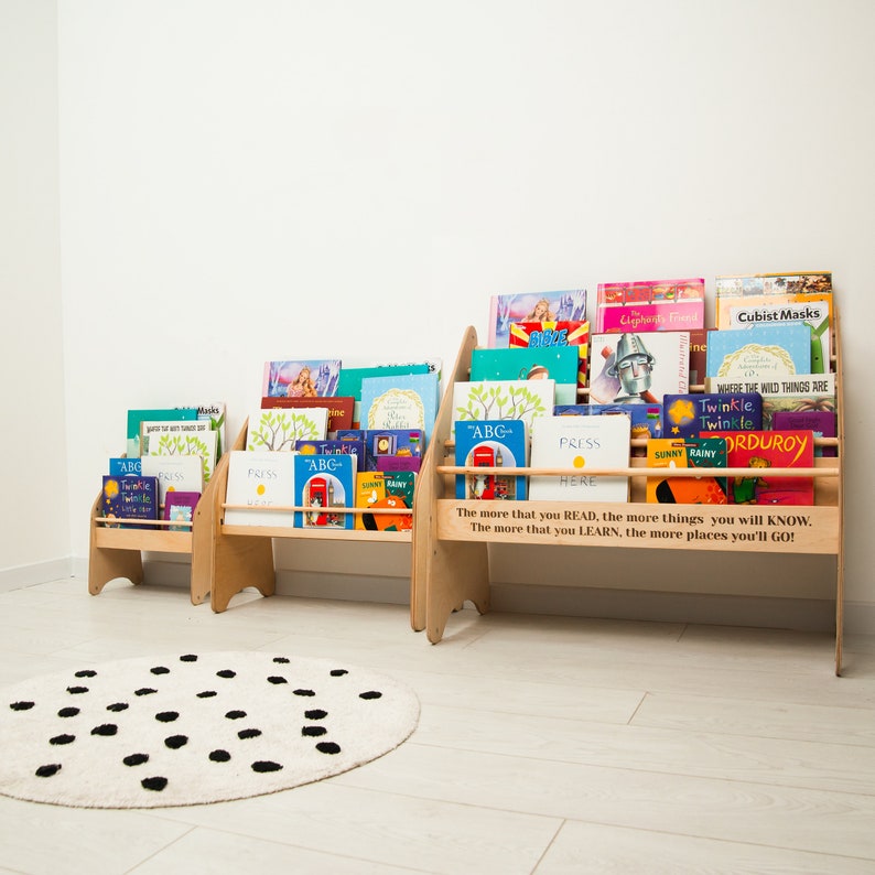 May include: Three wooden bookcases with colorful children's books on shelves. The bookcases are against a white wall and a black and white polka dot rug is in the foreground. The quote "The more that you READ, the more things you will KNOW. The more that you LEARN, the more places you'll GO!" is printed on the front of the largest bookcase.