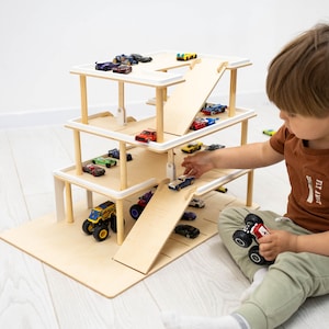 K&ouml;nnte beinhalten: Ein mehrst&ouml;ckiges Spielzeugparkhaus aus Holz mit Rampen und Parkpl&auml;tzen. Das Parkhaus ist mit verschiedenen Spielzeugautos in verschiedenen Farben gef&uuml;llt. Ein Kind spielt mit den Spielzeugautos.