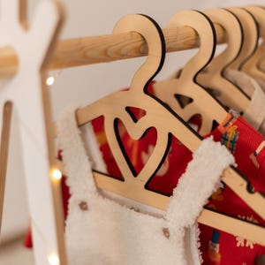 May include: Wooden hangers with a heart cut-out design, hanging on a wooden rack. The hangers are holding red and white clothing.