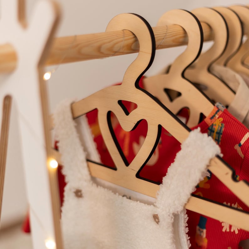May include: Wooden hangers with a heart cut-out design, hanging on a wooden rack. The hangers are holding red and white clothing.