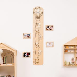 May include: A wooden growth chart featuring a hot air balloon design with the name "Amelia" at the top. The chart has teddy bears climbing along the side, with measurements in inches. Small framed photos are arranged around the chart.