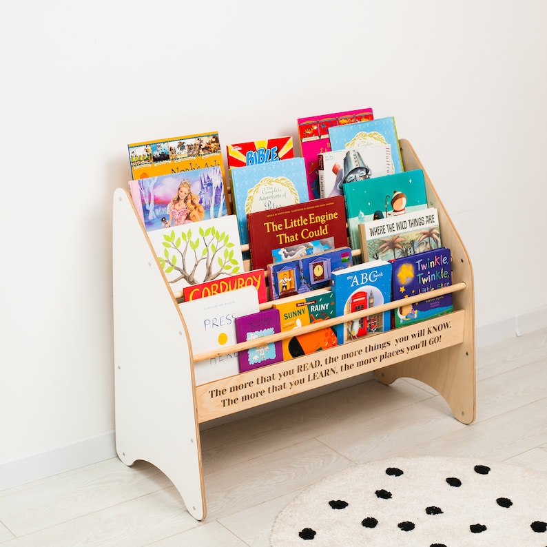May include: A white wooden bookshelf with a quote about reading and learning. The bookshelf is filled with colorful children's books, including "The Little Engine That Could", "Where the Wild Things Are", and "Corduroy".