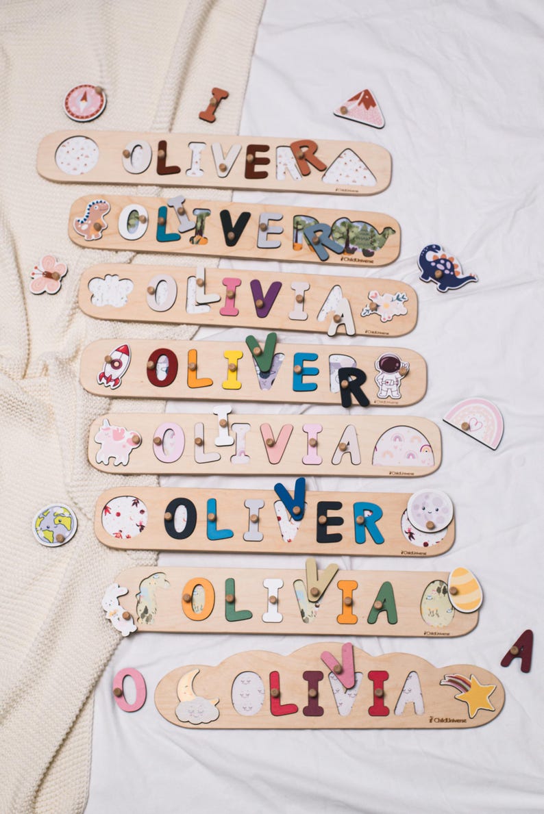 May include: Wooden name puzzles spelling "OLIVER" and "OLIVIA" in various colors. Each puzzle has a unique design, with decorative elements like dinosaurs, rockets, and rainbows. The puzzles are on a white surface.