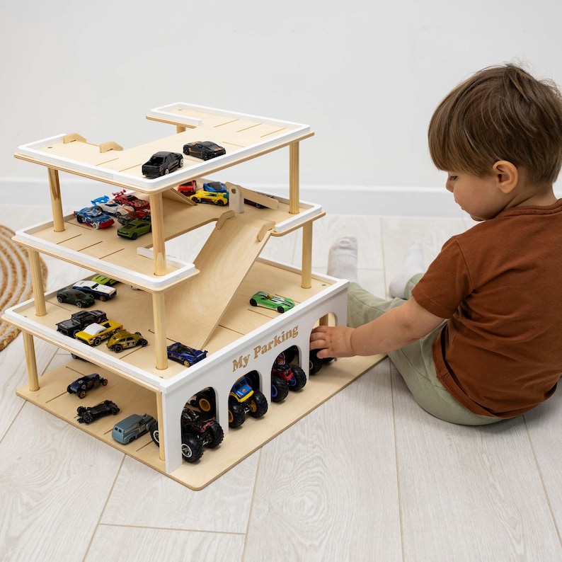 K&ouml;nnte beinhalten: Ein mehrst&ouml;ckiges Parkhaus aus Holz mit einer Rampe und mehreren Spielzeugautos. Das Parkhaus besteht aus hellem Holz mit wei&szlig;en Akzenten und tr&auml;gt den Schriftzug "My Parking" auf der Vorderseite.