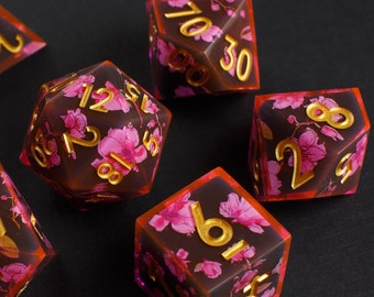 May include: Set of seven polyhedral dice with a dark brown and pink floral design. The dice are translucent and have gold numbers.