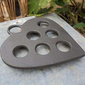 Peut inclure: Un dessous de plat en fonte noire en forme de cœur avec huit découpes rondes. Le dessous de plat est conçu pour maintenir les casseroles et les poêles chaudes.