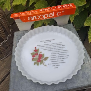 Puede incluir: Plato de tarta blanco con borde festoneado, diseño de frambuesas y texto de receta. El plato es de vidrio opal y tiene 27 cm de diámetro. Se ve una caja naranja y blanca con la marca "arcopal c".