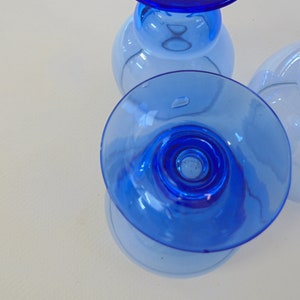 Op de afbeelding: Drie blauwe glazen bekers met een heldere basis en een blauwe rand. De bekers zijn op elkaar gestapeld.