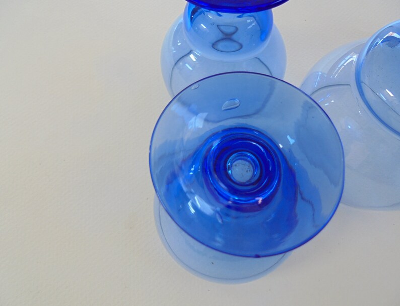 Op de afbeelding: Drie blauwe glazen bekers met een heldere basis en een blauwe rand. De bekers zijn op elkaar gestapeld.